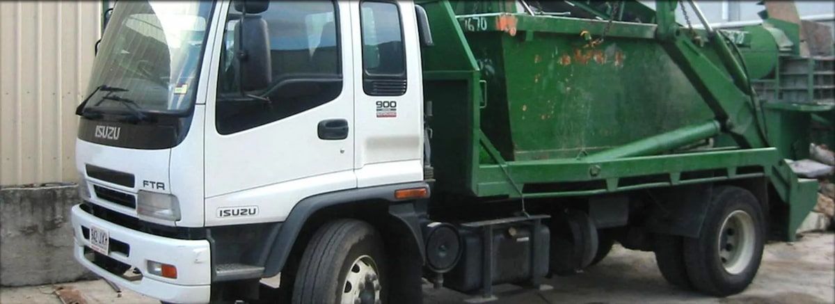 A White Isuzu Truck With a Green Skip Bin Attached, Parked Outdoors — Alice Skip Hire in Alice Springs, NT