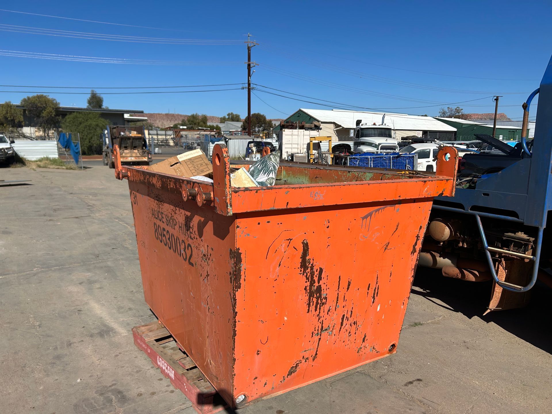Orange industrial dumpster in a yard with construction equipment and buildings in the background — Alice Skip Hire in Alice Springs, NT
