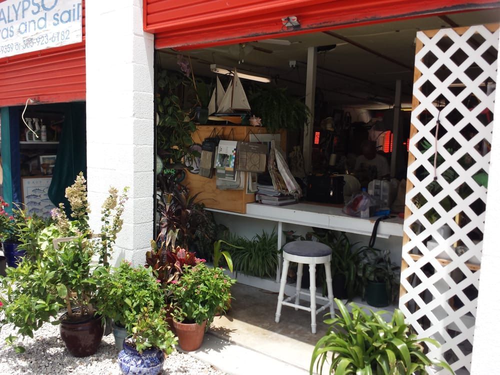 A tropical shop front with potted plants, a white stool, and a sailboat model displayed on a wooden counter.