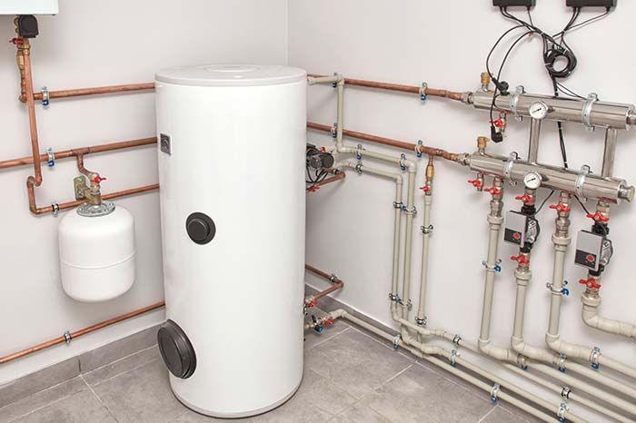 Boiler room with white water heater tank, copper pipes, and wall-mounted plumbing valves