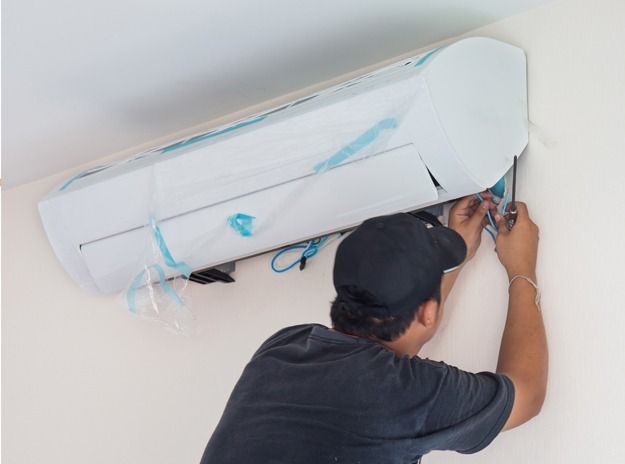 Technician repairing a wall-mounted air conditioner, with protective plastic covering and tools in hand