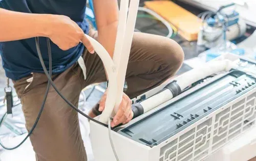 Technician installing an air conditioner unit with tools and cables open on a workbench