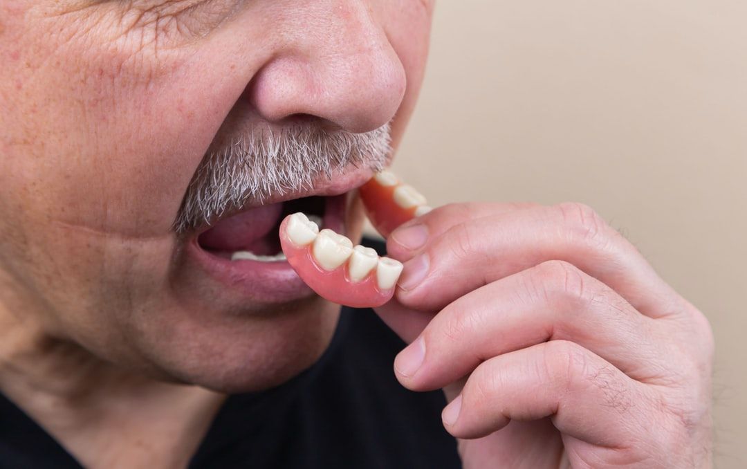 old gray haired man puts on partial dentures