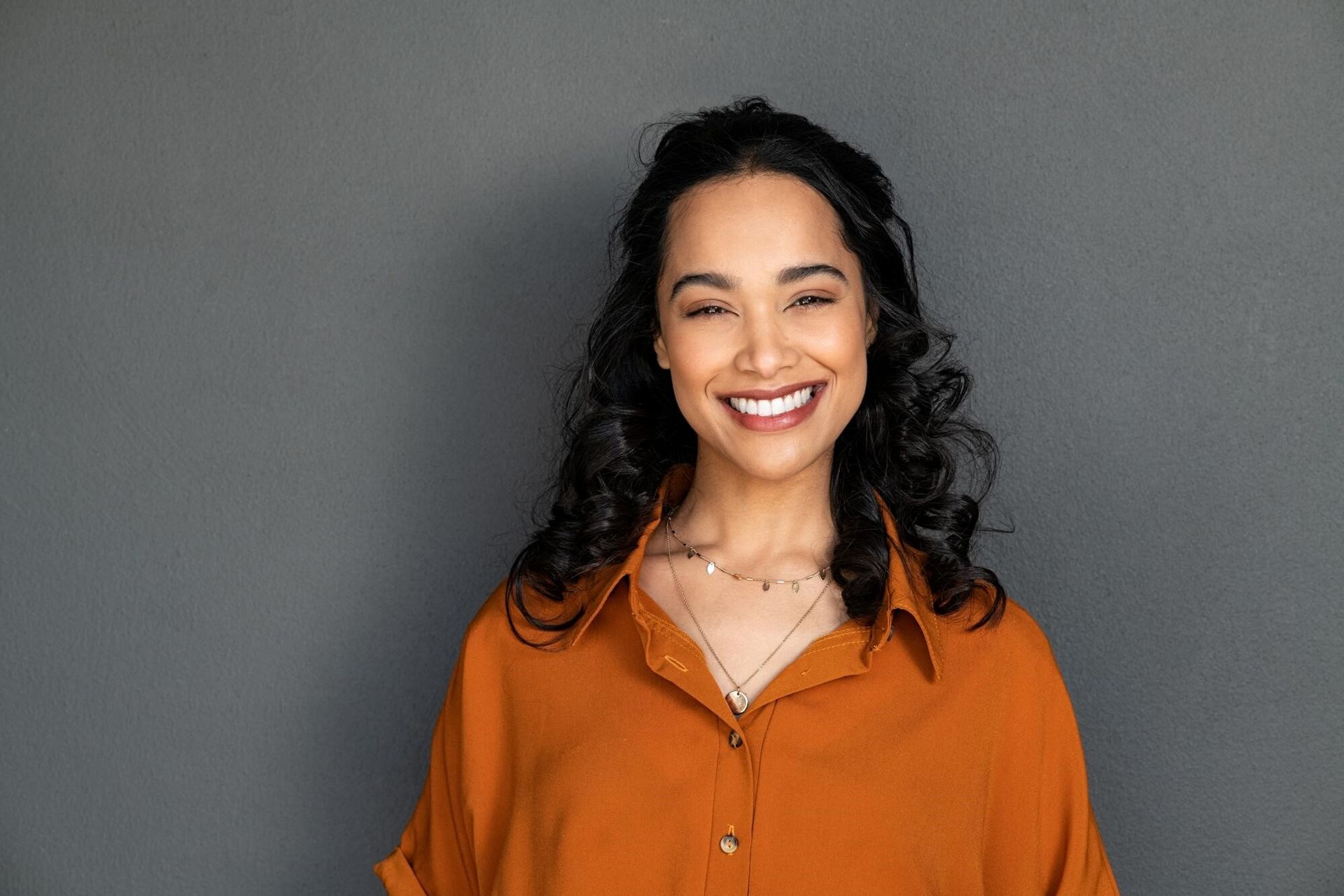 a woman in an orange shirt is smiling and looking at the camera .