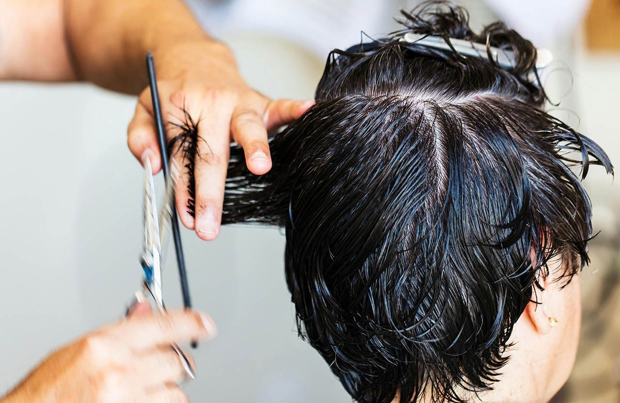 Kapper knipt nat, donker haar. Schaar in de hand, klant zit, bovenaanzicht.
