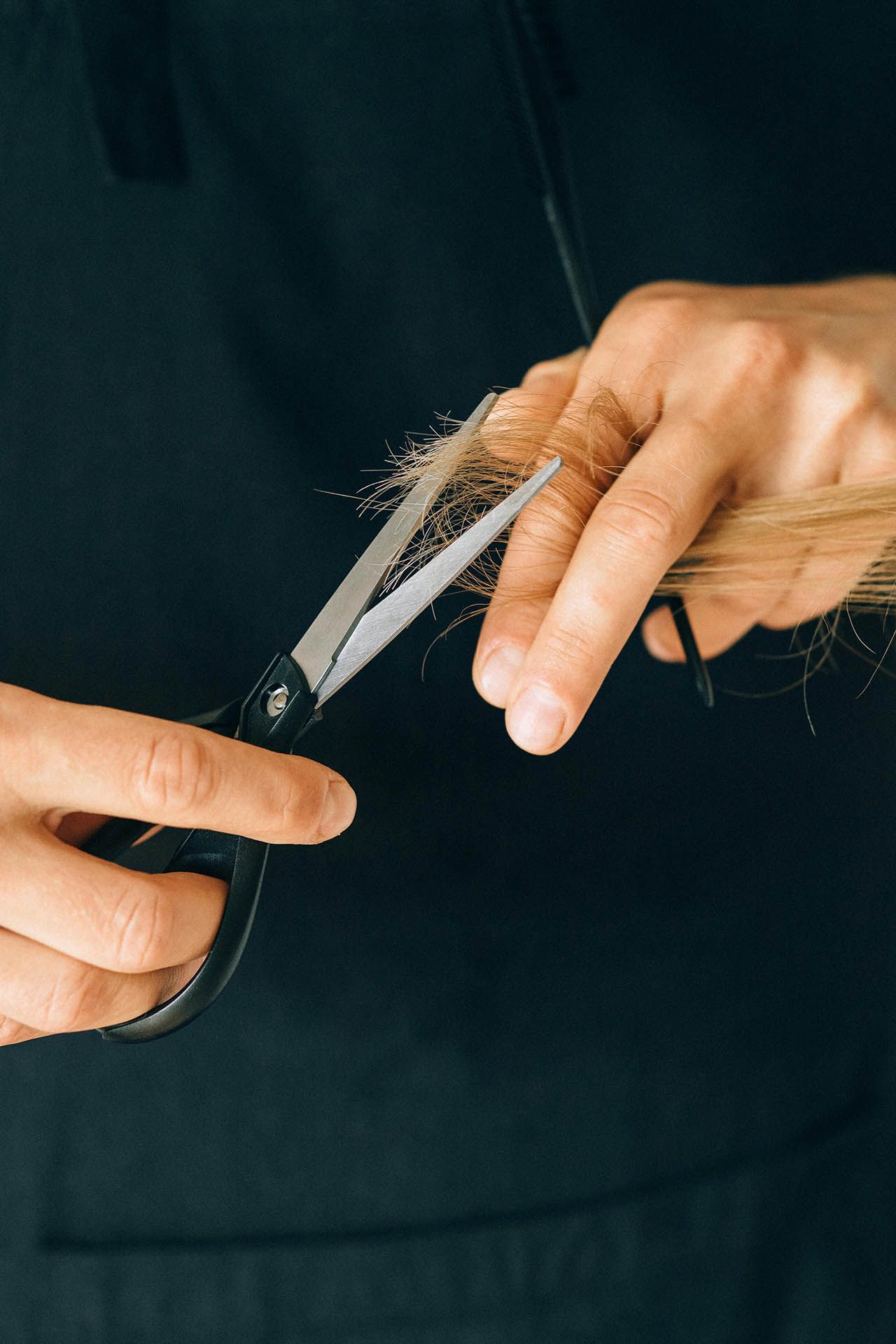 Iemand die met een schaar haar knipt, focus op handen en haar.