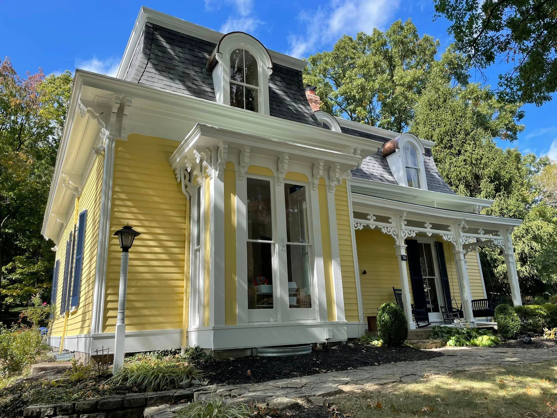 A small yellow house with a white porch and a blue sky in the background.