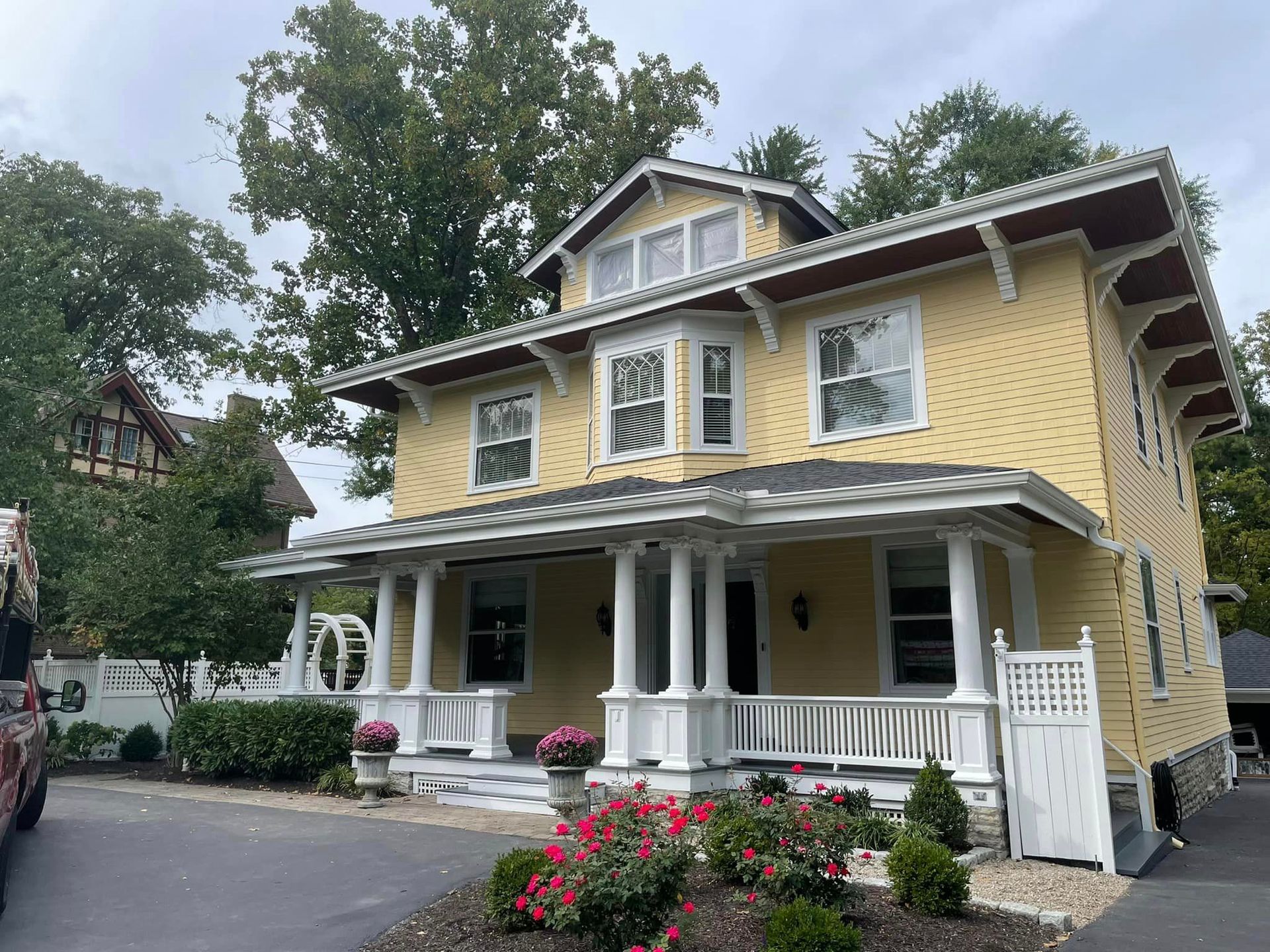 A large yellow house with a white porch and flowers in front of it.