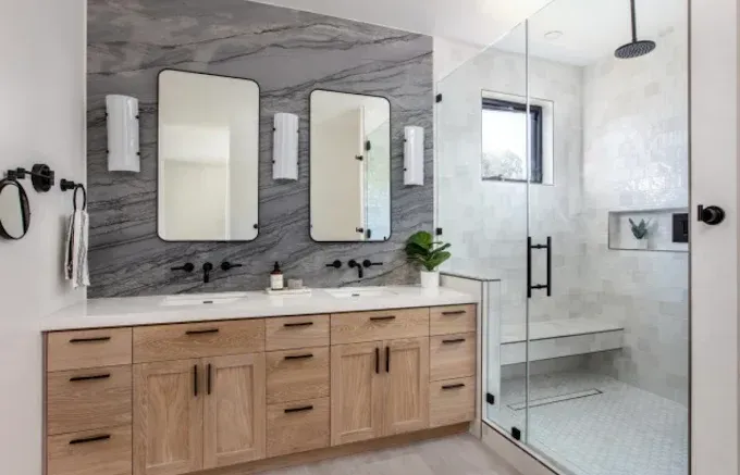 Modern bathroom with double vanity, glass shower, and gray marble accent wall.