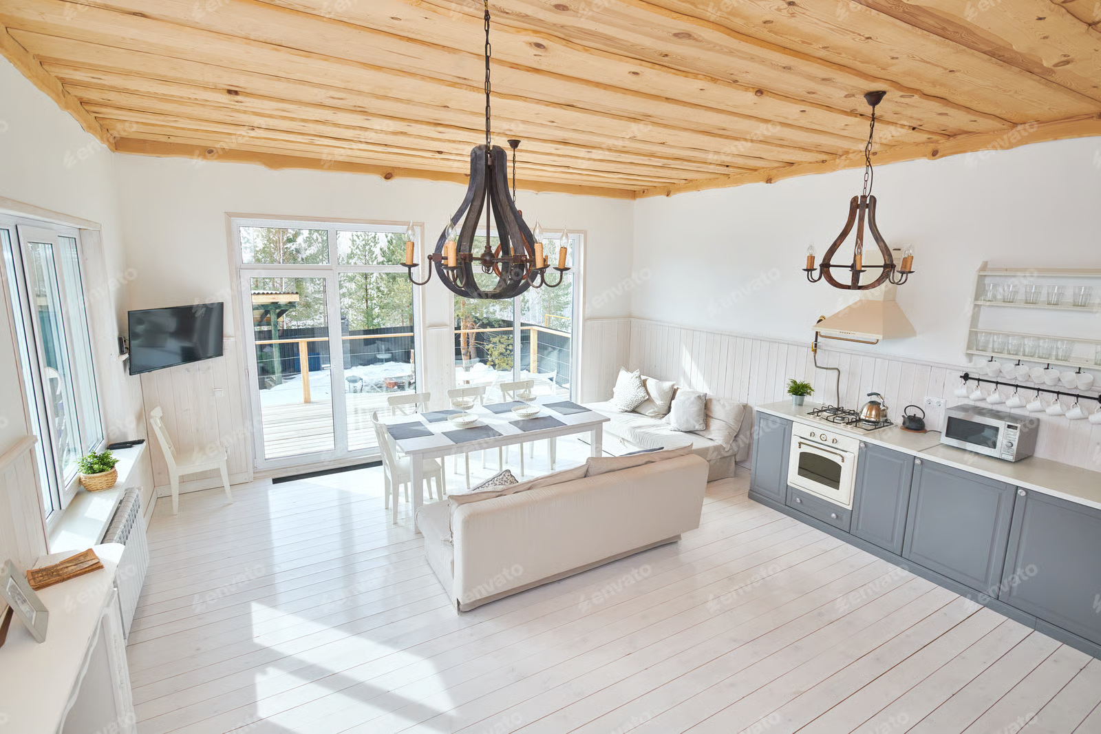 An open-plan living room with white wooden floors, a dining area, a grey kitchen, and a wooden ceiling with chandeliers.