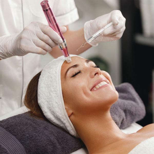 Cosmetische gezichtsbehandeling met een microneedling vlakbij het voorhoofd van een vrouw in een spa-omgeving.