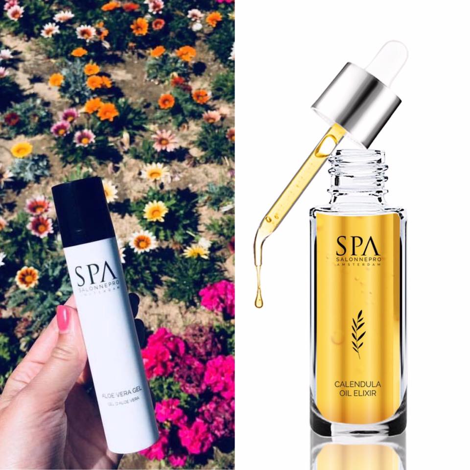 Hand houdt een flesje SPA-huidverzorgingsproducten vast, naast een open pipetje met calendula-olie boven bloemen.