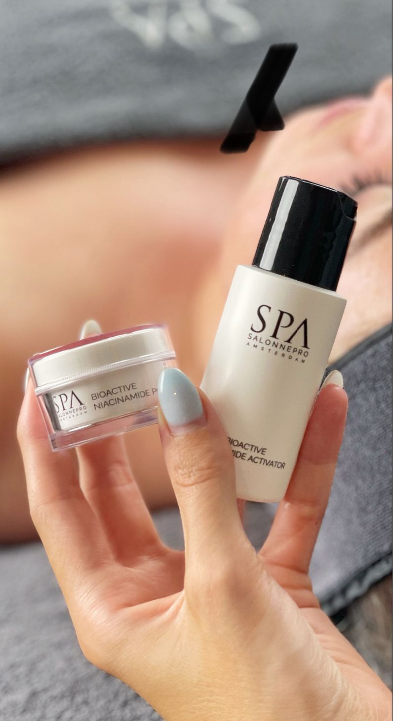 Hand die een flesje SPA-huidverzorgingsproducten en een potje crème vasthoudt, met een sprayflacon op de achtergrond.