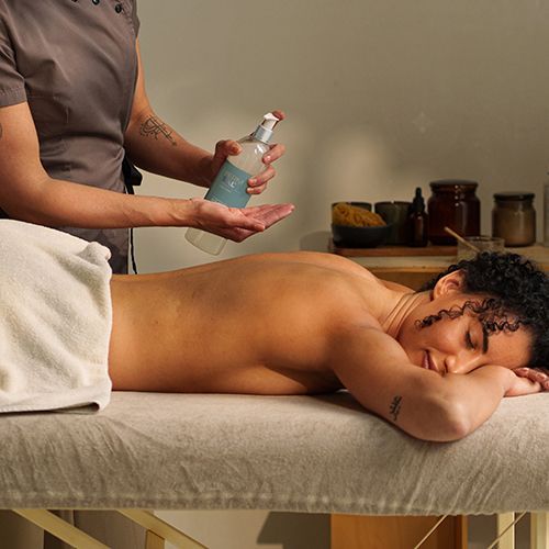 Een massagetherapeut spuit olie op een cliënt die met het gezicht naar beneden op een massagetafel ligt.
