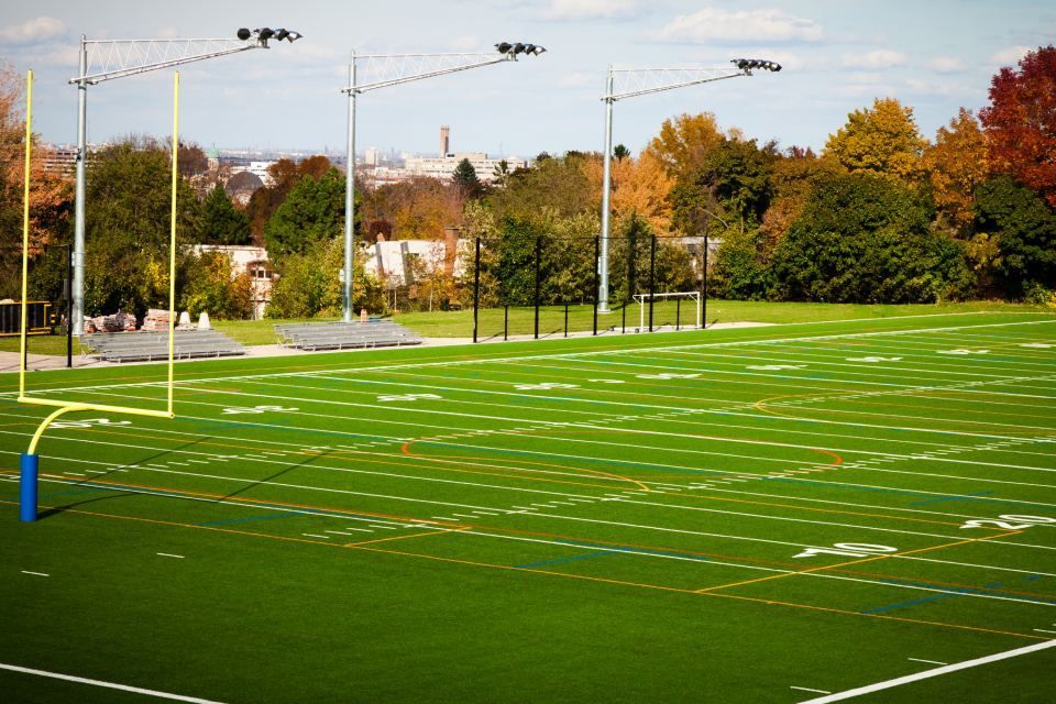 Empty green sports field with white yard lines and tall lights beside autumn trees