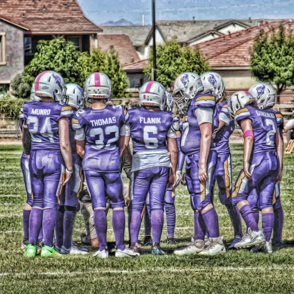 Youth football team in purple uniforms huddling on a grassy field before a game.