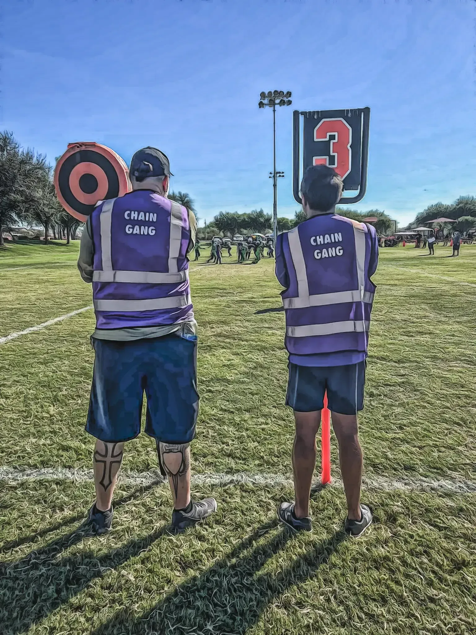 Two people in purple safety vests stand on grass at an outdoor shooting range with target signs.