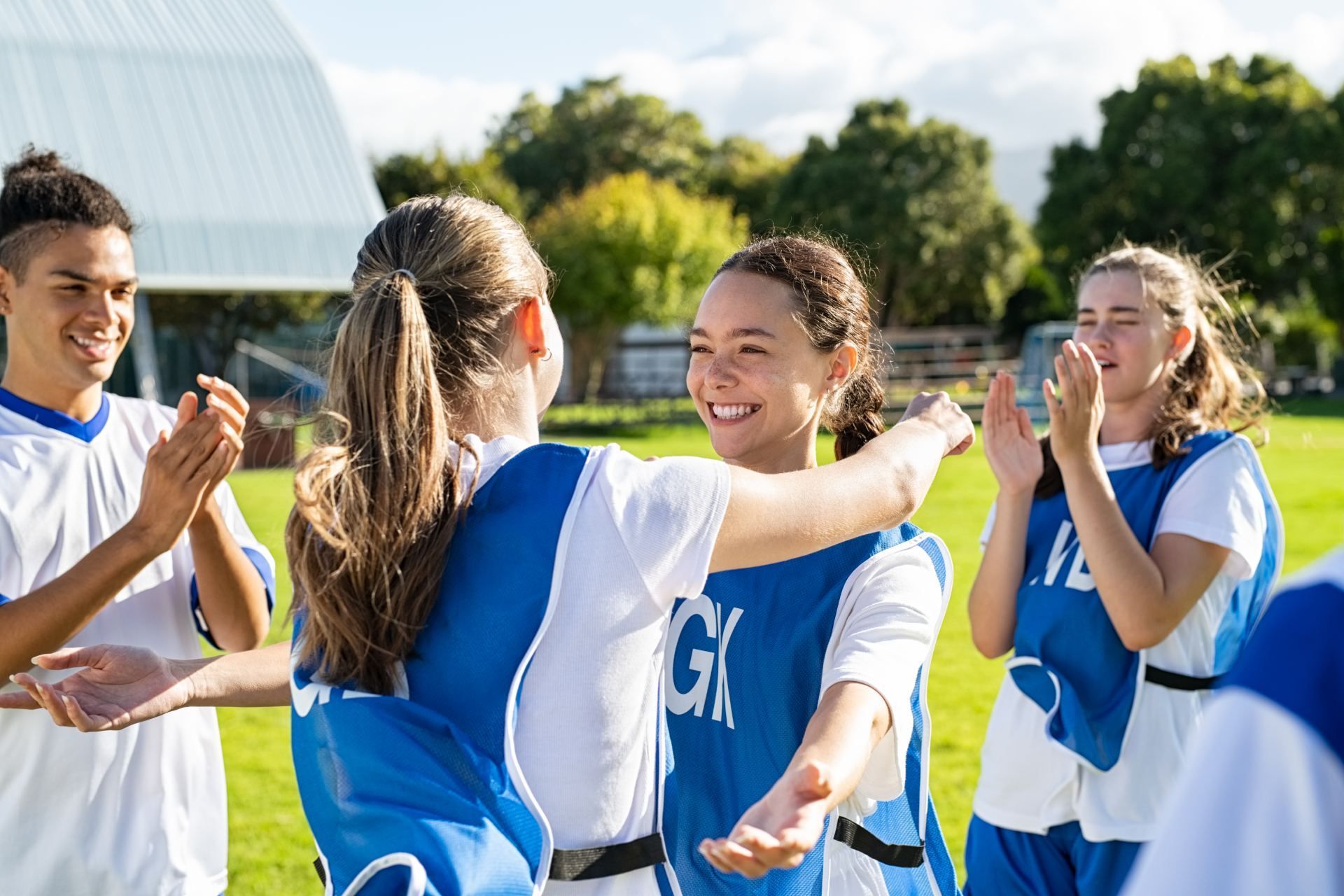 Youth soccer players in blue jerseys celebrating together on a sunny field