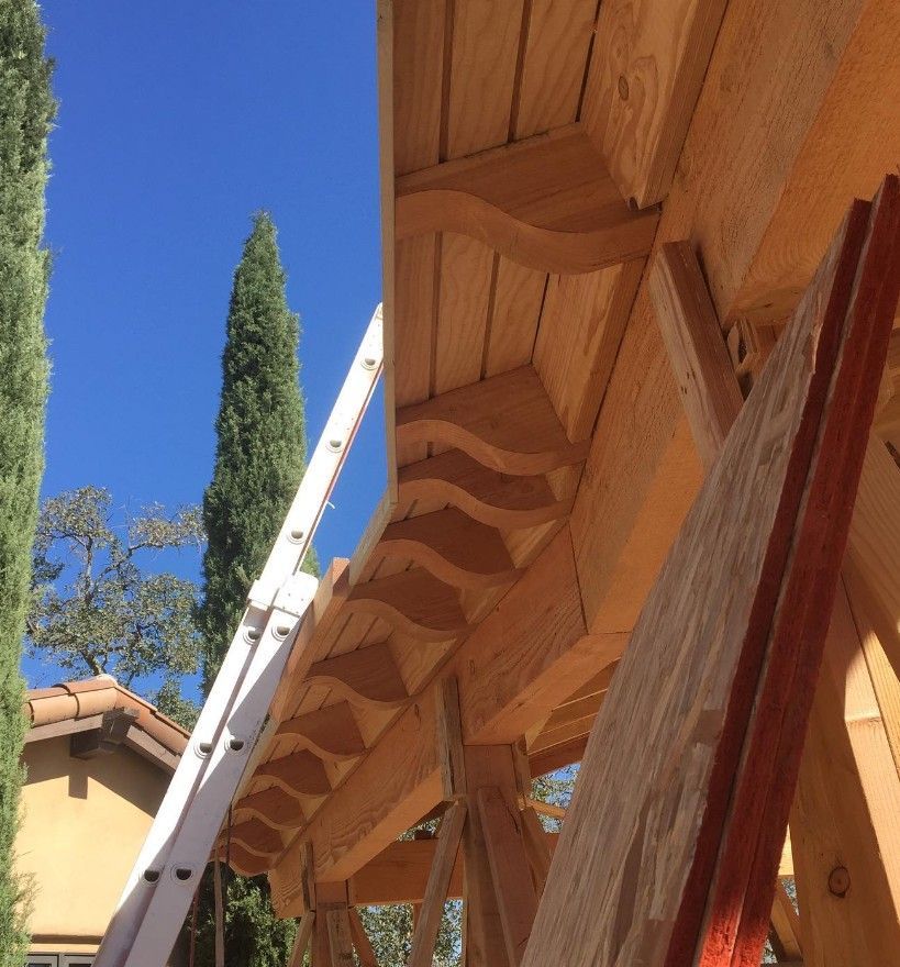 Ladder leaning against a wooden roof eave beside a house under a blue sky