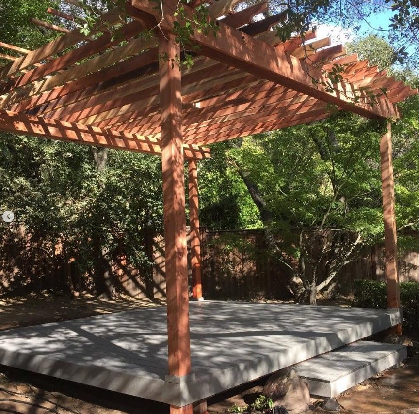 Wooden pergola over a raised deck in a leafy backyard, with stone steps on the right.