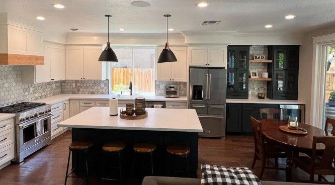 Modern kitchen with white island, black pendant lights, stainless appliances, and a small dining table.