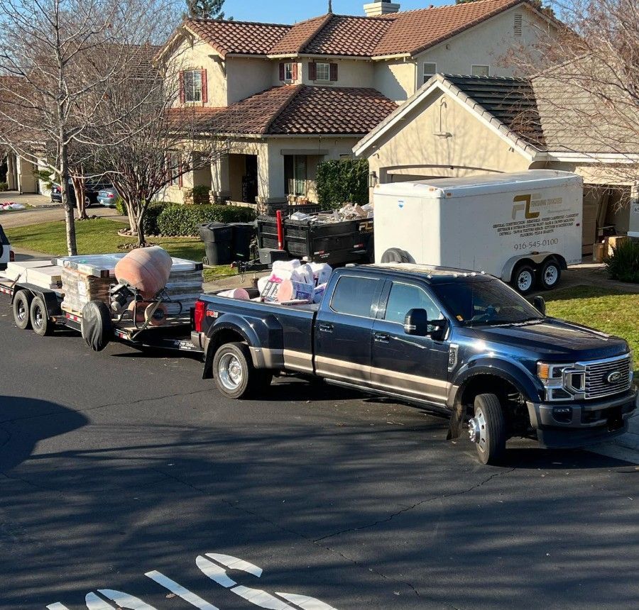 Black pickup truck towing a small trailer on a suburban street with houses in the background