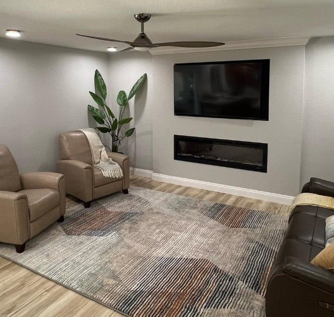 Modern living room with beige chairs, wall-mounted TV, fireplace, large rug, and potted plant