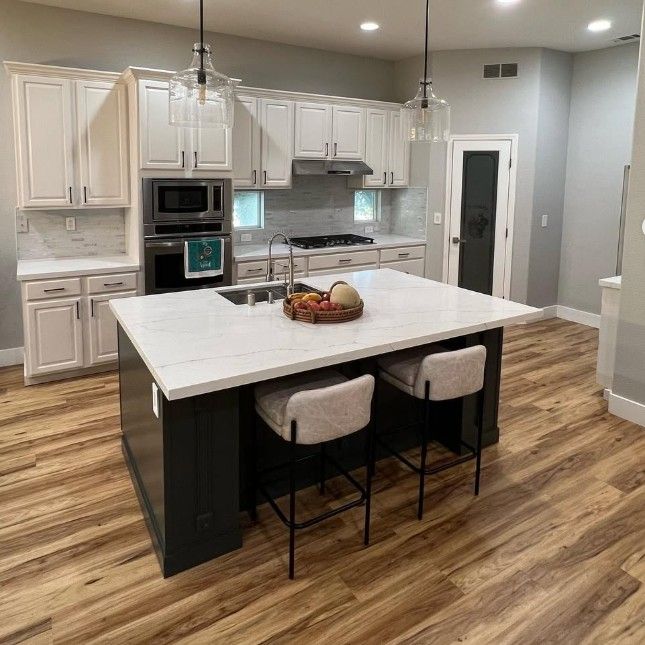 Modern kitchen with white cabinets, large island, stainless appliances, and wood-look flooring.