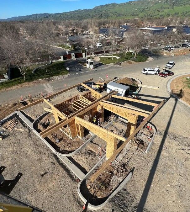 Aerial view of a wooden house foundation under construction beside a road in a hilly area