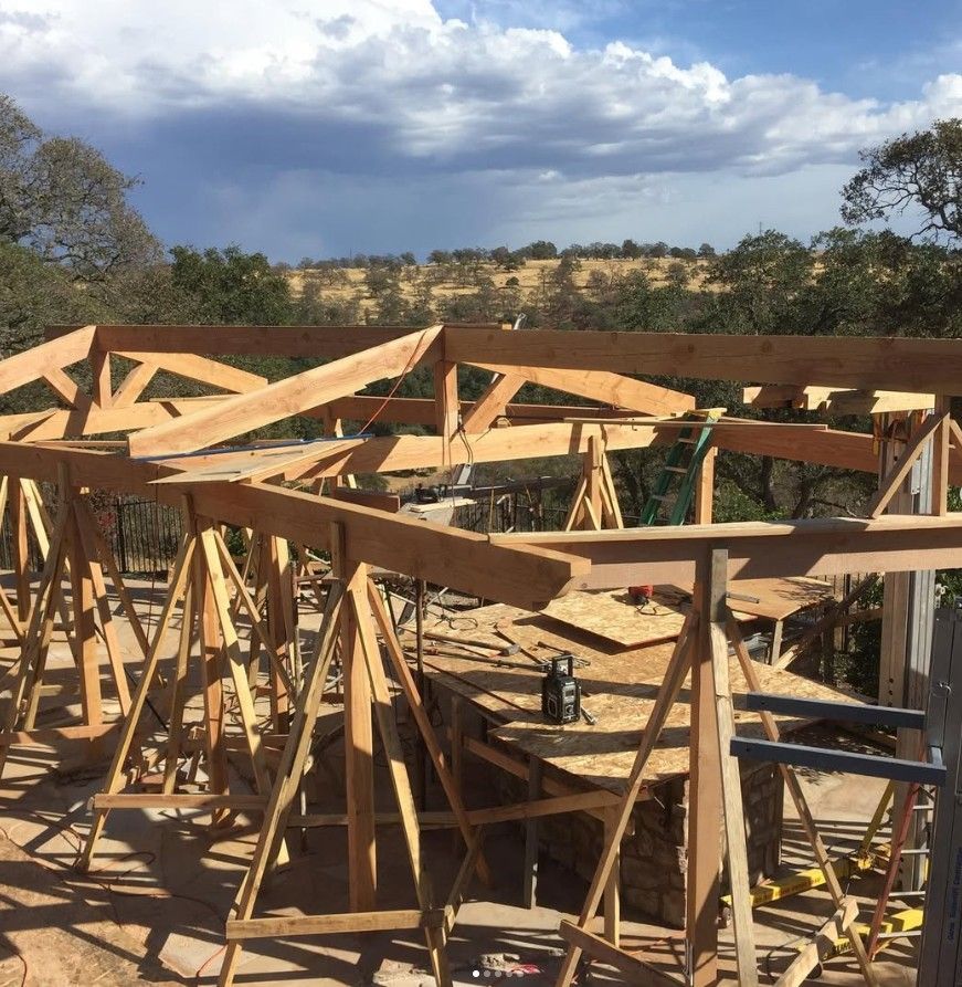 Wooden roof trusses under construction at an outdoor building site with hills in the background