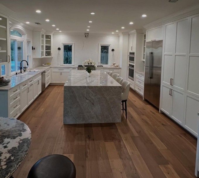 Modern white kitchen with a large marble island, hardwood floors, and stainless steel appliances