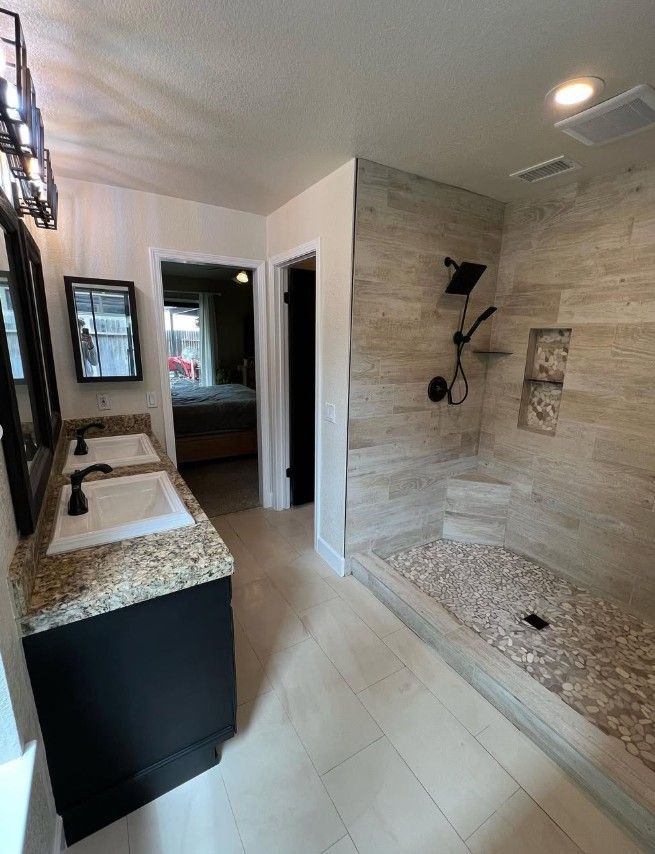 Modern bathroom with double vanity, large tiled walk-in shower, and light stone finishes.