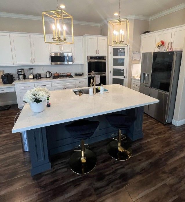 Modern white kitchen with a large marble island, dark blue base, pendant lights, and stainless steel appliances