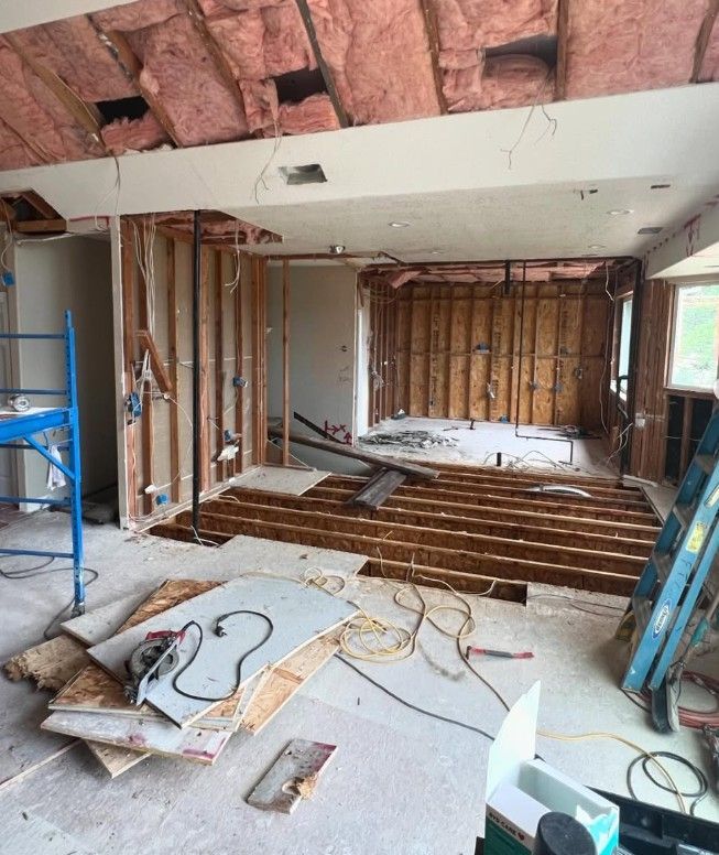 Interior under renovation with exposed beams, framing, wiring, and construction debris on the floor