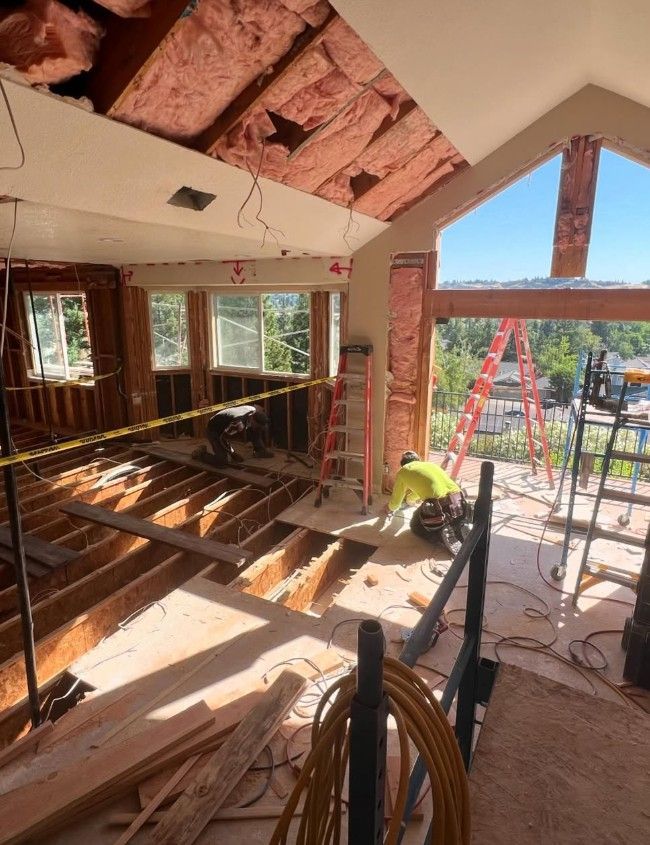 Interior renovation with exposed ceiling beams, ladders, tools, and workers near open wall framing
