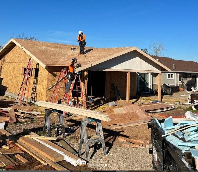 Workers repairing a house roof and exterior amid construction debris on a sunny day