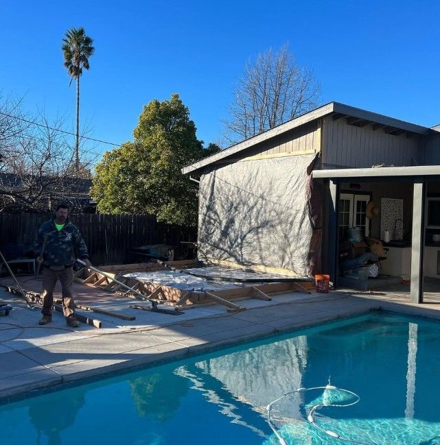 Person working beside a backyard pool near a house, with a palm tree and blue sky in the background