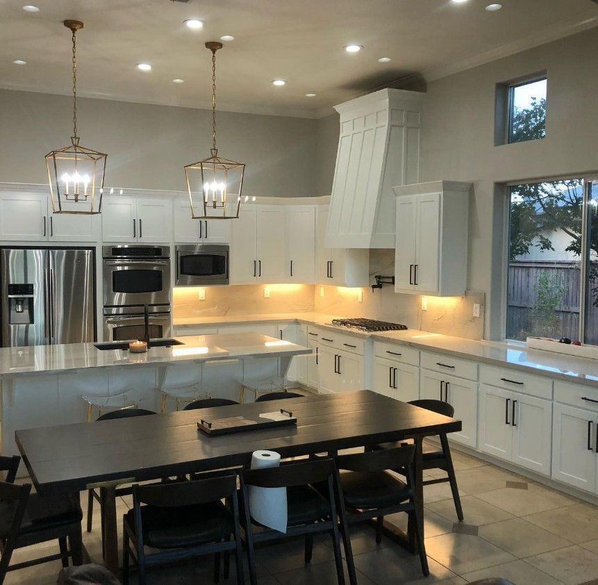 Bright modern kitchen with white cabinets, stainless appliances, island, and black dining table