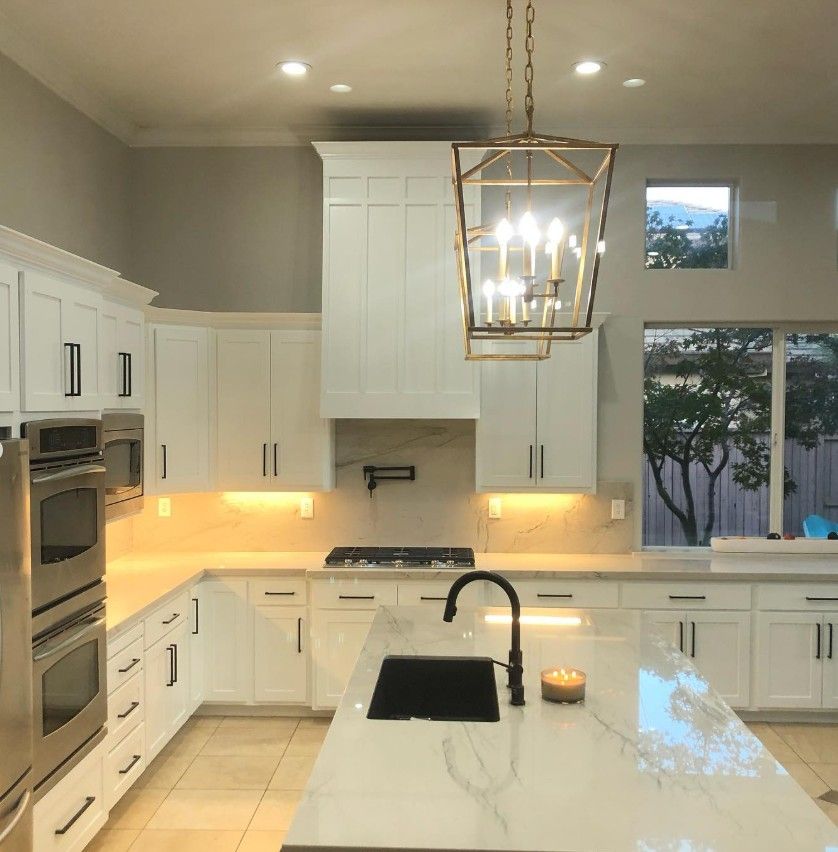 Bright white modern kitchen with island, black sink, gold lantern light, and large window