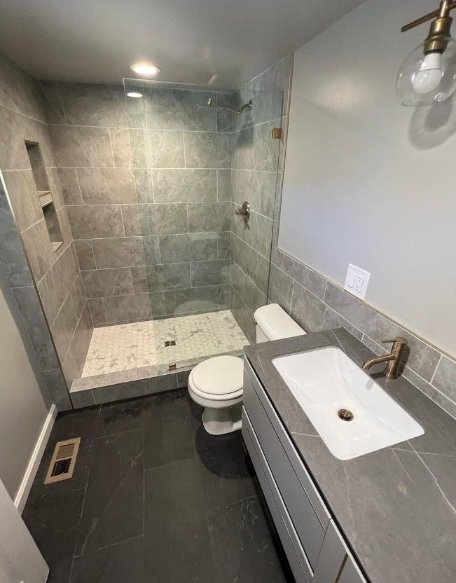 Modern bathroom with walk-in stone shower, gray vanity, white sink, and dark tile floor