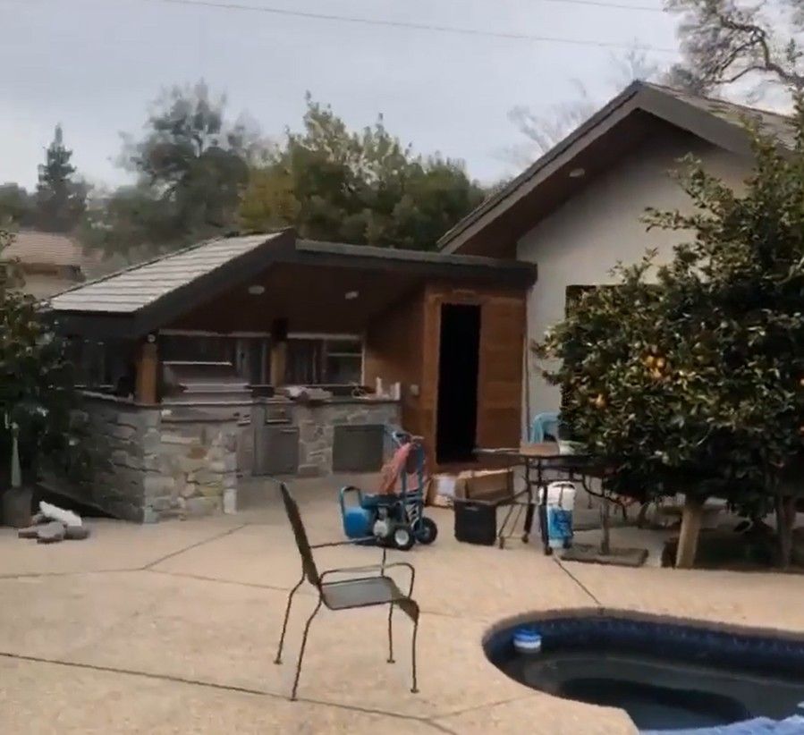 Backyard patio with a stone grill, toy wagon, chairs, and a small pool in the foreground