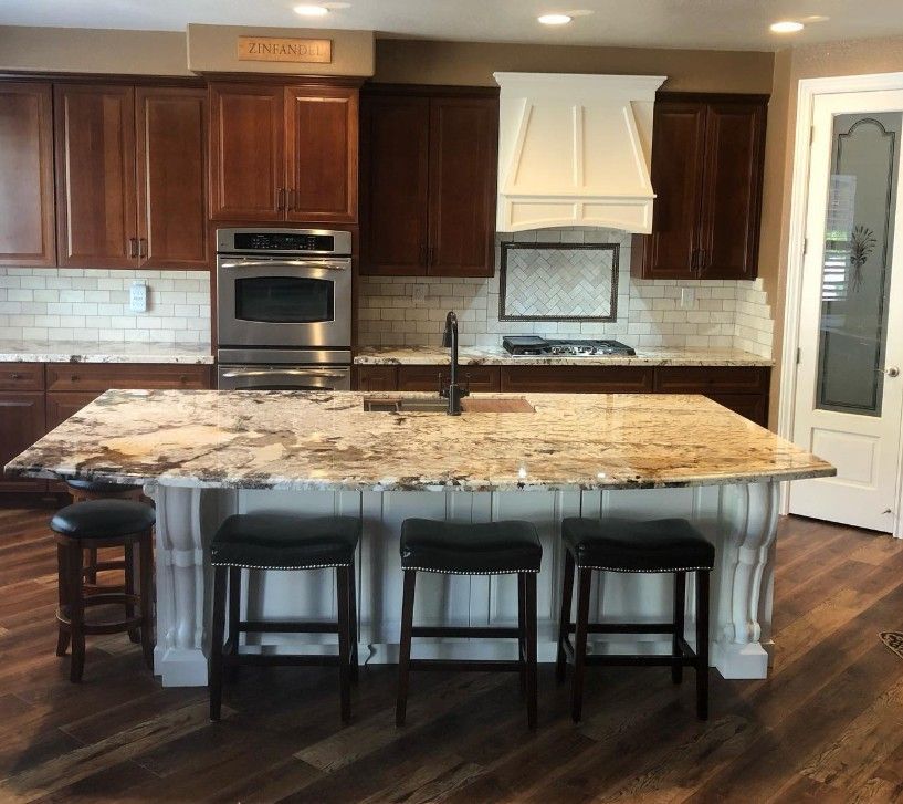 Modern kitchen with granite island, dark wood cabinets, stainless oven, and four stools