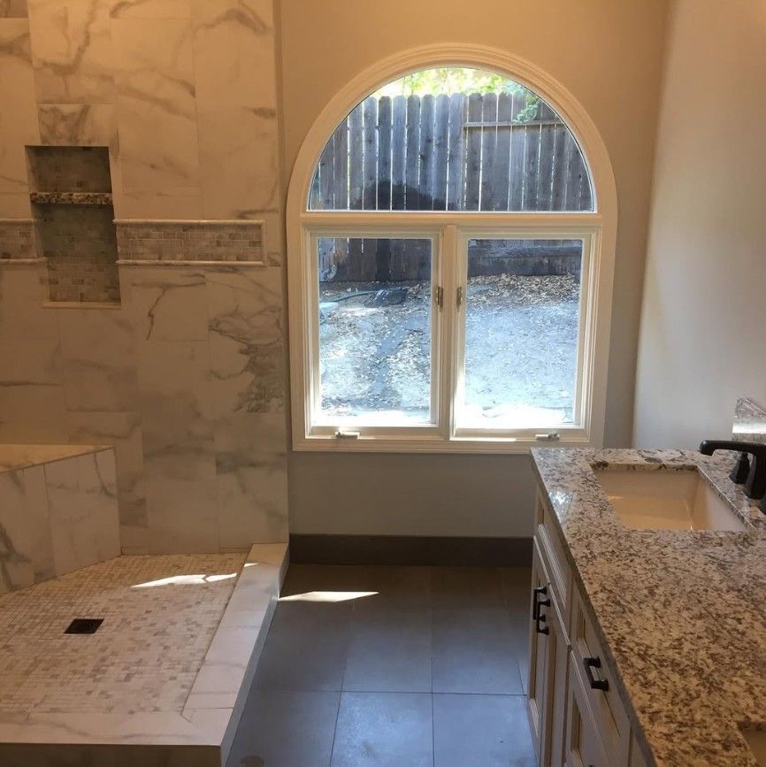 Empty bathroom with marble tile shower, vanity, and arched window overlooking a snowy yard