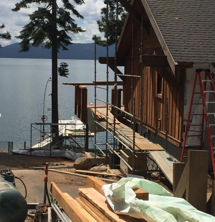 Wooden lakeside cabin under construction with scaffolding, lumber, and tools by the water
