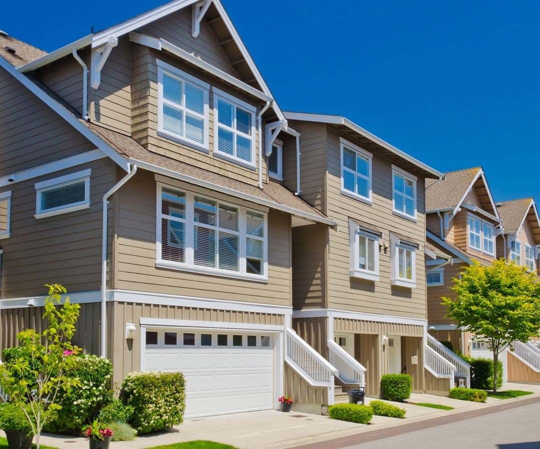 Row of tan townhouses with white trim and garage doors on a sunny day.