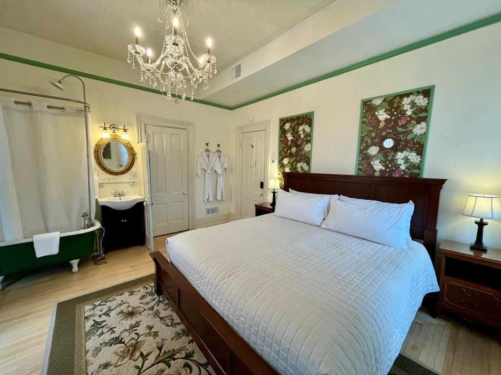 A bedroom with a king size bed and a green tub.