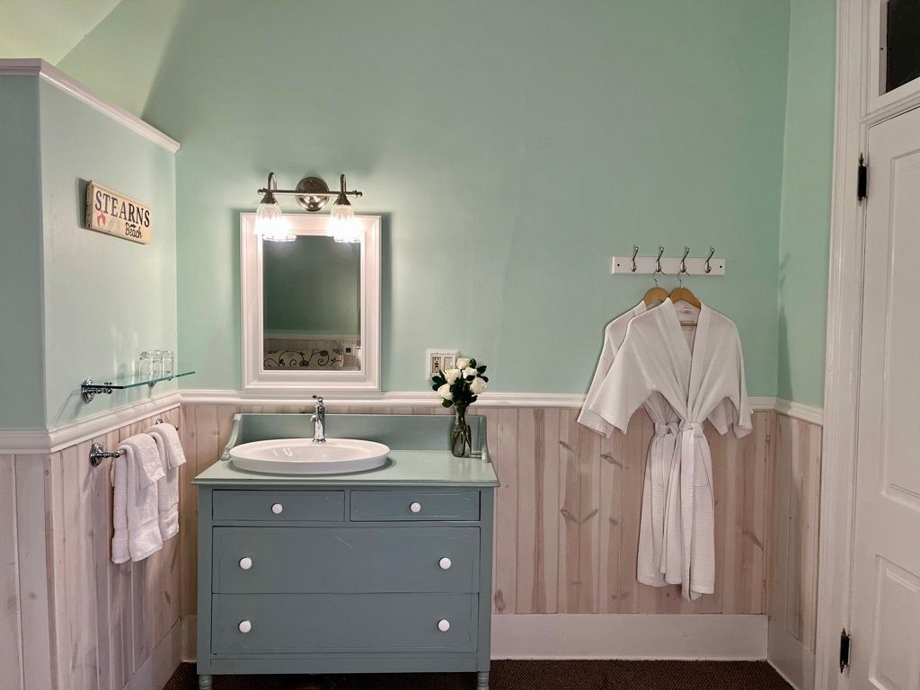 A bathroom with a sink , mirror and robes hanging on the wall.