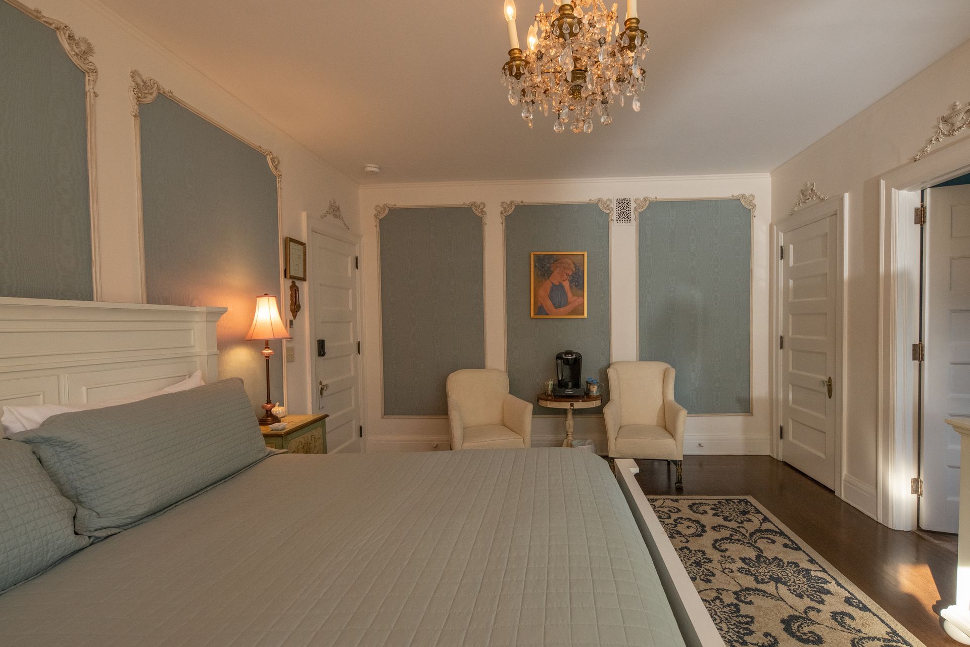 A bedroom with a large bed , chairs and a chandelier.