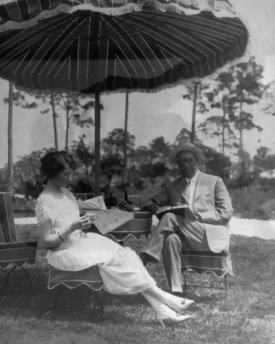 A black and white photo of a man and woman sitting under an umbrella