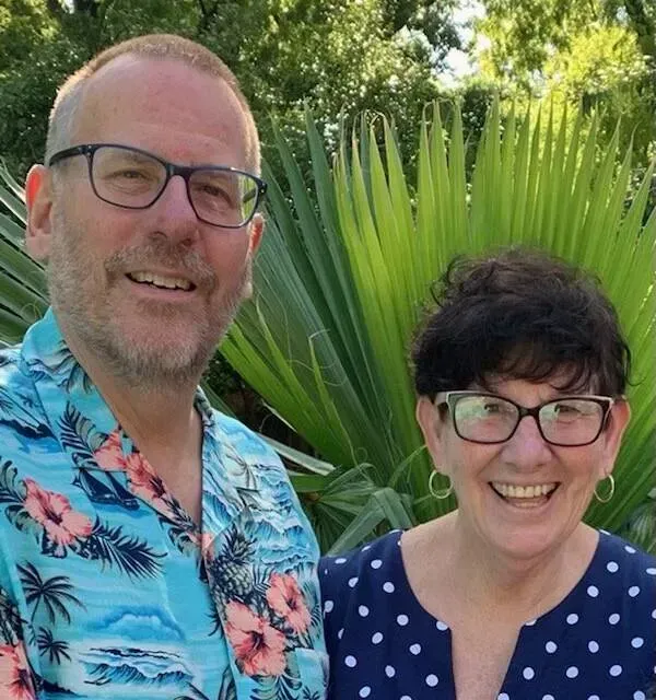A man and a woman are posing for a picture in front of a palm tree.
